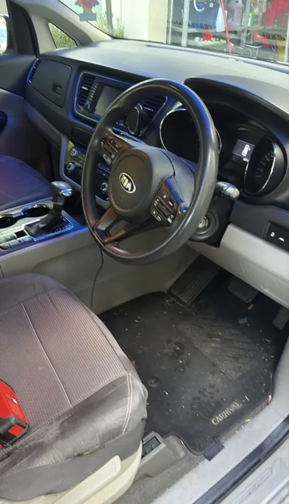 Kia Carnival front seat and floor mat before an interior detail, with dirt and leaves on the carpet